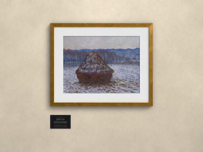 May include: A framed print of an impressionist painting featuring a dark brown haystack in a snow-covered field under a pale sky. The artwork is enclosed in a gold-colored frame with a white mat. A small black plaque with white text is below.