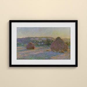 May include: A framed landscape painting featuring two large haystacks in a field under a soft, hazy sky. The artwork displays a palette of muted purples, greens, and yellows, enclosed within a simple black frame and a white mat border.