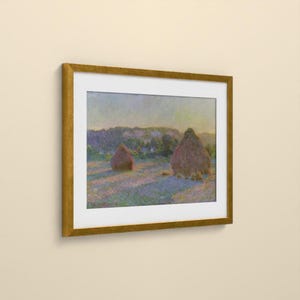 May include: A framed landscape painting featuring two large haystacks in a field during sunset. The artwork displays soft brushstrokes in shades of purple, blue, and gold, enclosed within a simple, metallic gold-colored rectangular frame.