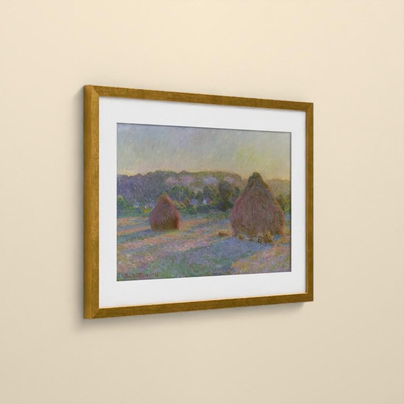 May include: A framed landscape painting featuring two large haystacks in a field during sunset. The artwork displays soft brushstrokes in shades of purple, blue, and gold, enclosed within a simple, metallic gold-colored rectangular frame.