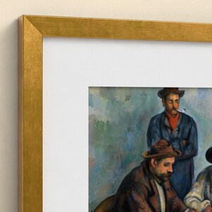 May include: A framed art print featuring a painting of two figures in hats. The top figure wears a blue coat and red scarf with a pipe in their mouth. The bottom figure wears a brown coat. The frame is a metallic gold with a white mat border.