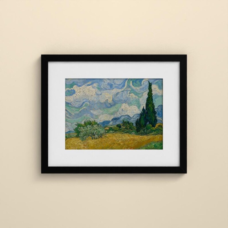 May include: A framed art print featuring a landscape painting with a golden wheat field, a tall dark green cypress tree, and a swirling blue and white sky. The artwork is enclosed in a simple black frame with a white mat border.