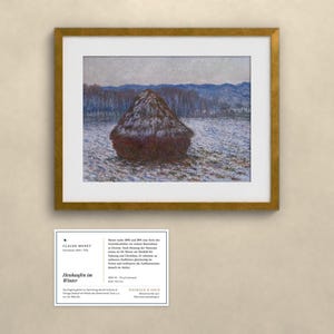 May include: A framed print of Claude Monet's painting Heubaufen im Winter, featuring a dark haystack in a snowy field with blue hills in the background. Below the frame is an informational card with text about the artwork and the artist.