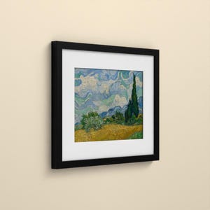 May include: A framed square art print featuring a landscape painting with a golden yellow wheat field, a dark green cypress tree, and a swirling blue and white sky. The artwork is encased in a simple black frame with a wide white mat border.