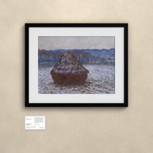 May include: A framed print of an impressionist painting depicting a dark brown haystack in a snowy field under a pale sky. The artwork is enclosed in a black frame with a white mat. Below the frame is a small white informational placard.