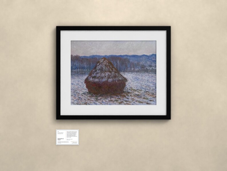 May include: A framed print of an impressionist painting depicting a dark brown haystack in a snowy field under a pale sky. The artwork is enclosed in a black frame with a white mat. Below the frame is a small white informational placard.