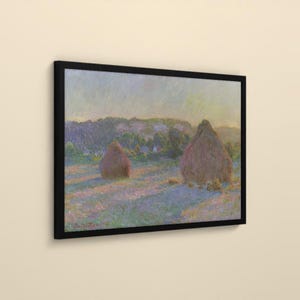 May include: A framed landscape painting featuring two large haystacks in a field under a soft, hazy sky. The scene uses a palette of muted purples, blues, and golden yellows, with a dark black frame surrounding the rectangular canvas.