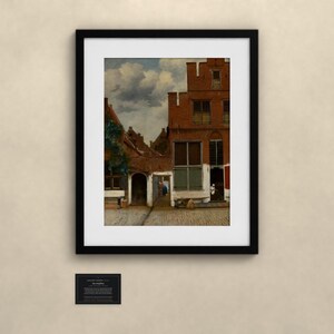 May include: A framed art print depicting a Dutch Golden Age street scene with red brick buildings, a cobblestone path, and a cloudy sky. The painting features a tall gabled house, a central archway, and a small figure standing in a doorway.
