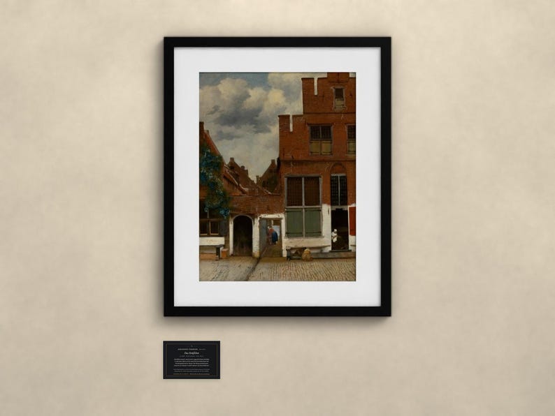 May include: A framed art print depicting a Dutch Golden Age street scene with red brick buildings, a cobblestone path, and a cloudy sky. The painting features a tall gabled house, a central archway, and a small figure standing in a doorway.