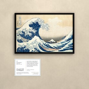 May include: A framed print of The Great Wave off Kanagawa featuring a large blue cresting wave, boats with rowers, and Mount Fuji in the distance. Below the print is an informational card with text detailing the artwork's history.