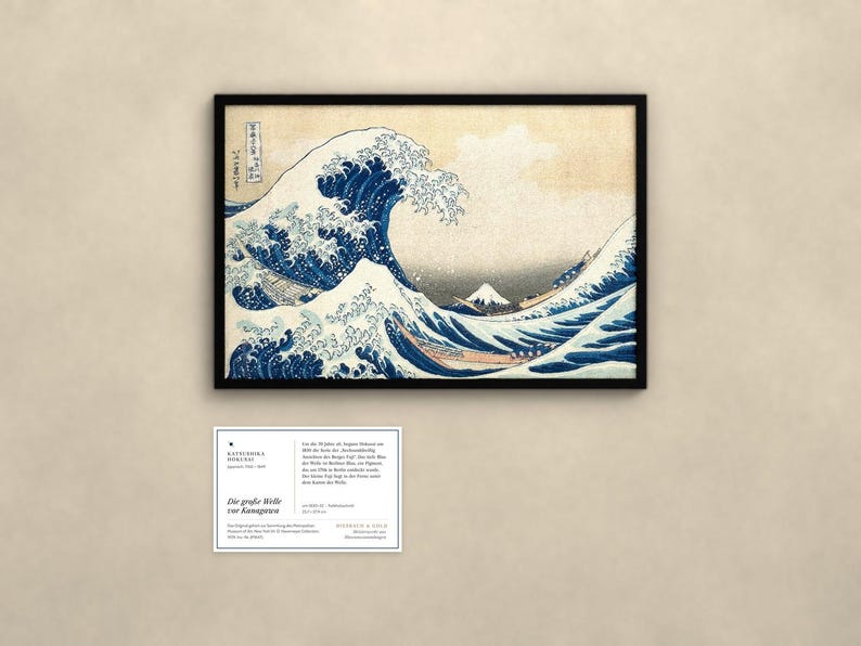 May include: A framed print of The Great Wave off Kanagawa featuring a large blue cresting wave, boats with rowers, and Mount Fuji in the distance. Below the print is an informational card with text detailing the artwork's history.