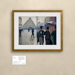 May include: A framed print of the painting Paris Street; Rainy Day, showing figures in 19th-century clothing holding umbrellas on a cobblestone street lined with tall buildings. A small informational plaque is mounted below the frame.