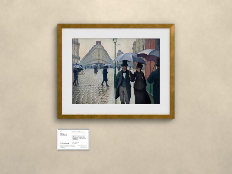 May include: A framed print of the painting Paris Street; Rainy Day, showing figures in 19th-century clothing holding umbrellas on a cobblestone street lined with tall buildings. A small informational plaque is mounted below the frame.