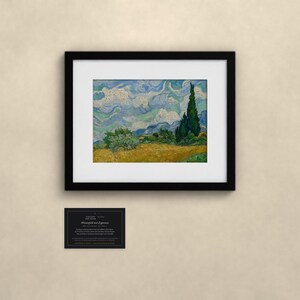 May include: A framed print of Vincent van Gogh's Wheat Field with Cypresses, featuring a golden wheat field, dark green cypress trees, and a swirling blue sky. Below the frame is a small black rectangular card with white text.