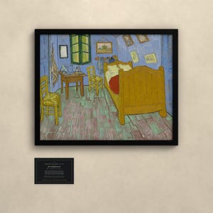 May include: A framed print of Vincent van Gogh's Bedroom in Arles painting, featuring a yellow bed, two chairs, and a small table in a blue room. Below the frame is a small black plaque with white text detailing the artwork's history.