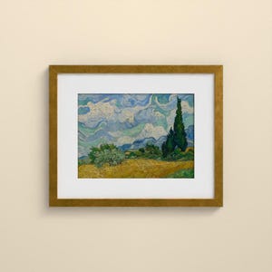 May include: A framed art print featuring a landscape painting with a golden yellow wheat field, a dark green cypress tree, and a swirling blue and white sky. The artwork is enclosed in a simple gold-toned frame with a white mat border.