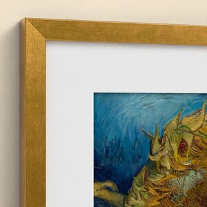 May include: A framed art print featuring a section of a painting with yellow sunflowers against a deep blue background. The artwork is encased in a white mat and a metallic gold frame with a flat, clean-lined profile and mitered corners.