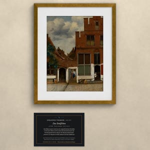 May include: A framed print of Johannes Vermeer's painting The Little Street, depicting a red brick Dutch house facade with a cobblestone alleyway under a cloudy sky, accompanied by a black informational plaque with white text.