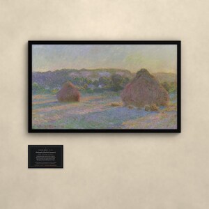 May include: A framed landscape painting featuring two large haystacks in a field under a soft sky, with a small black informational plaque below. The artwork displays muted tones of purple, gold, and green, capturing a rural scene.