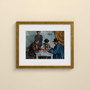 May include: A framed art print depicting a painting of four individuals wearing hats gathered around a white table. Three individuals are seated playing cards, while one stands behind them. The scene features muted blue, brown, and gold tones in a gold-colored frame.