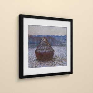 May include: A framed print featuring an impressionist painting of a dark brown haystack centered in a snowy field. The background displays blue-toned trees and distant mountains under a pale sky, all enclosed in a simple black frame.