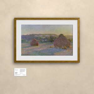 May include: A framed landscape painting featuring two large haystacks in a field under a soft sky, rendered in impressionistic brushstrokes of purple, gold, and green. A small white informational placard is positioned below the framed artwork.