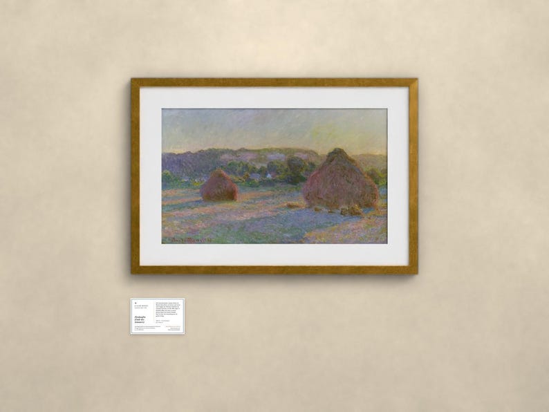 May include: A framed landscape painting featuring two large haystacks in a field under a soft sky, rendered in impressionistic brushstrokes of purple, gold, and green. A small white informational placard is positioned below the framed artwork.