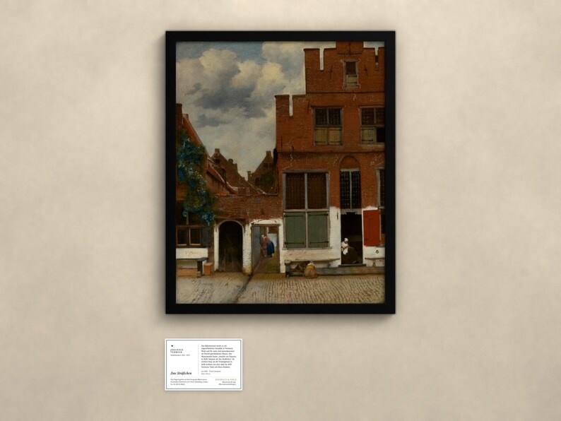 May include: A framed print of a painting depicting a Dutch courtyard with red brick buildings, a cobblestone ground, and a cloudy sky. A small white information card is positioned below the frame, containing text about the artwork.