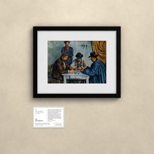 May include: A framed art print of Paul C&eacute;zanne's The Card Players, featuring four figures seated around a table. The painting is enclosed in a black frame with a white mat. Below the frame is a small white informational card with text.