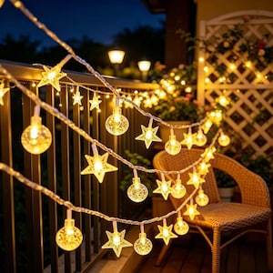 May include: A string of outdoor LED lights featuring alternating clear spherical globes and five-pointed star shapes. The lights emit a warm yellow glow and are draped along a dark railing at night, creating a decorative illumination effect.