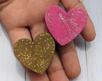 May include: Two heart-shaped decorations with glitter. One heart is pink with silver glitter, and the other is brown with gold glitter.