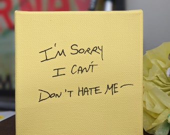May include: A yellow canvas with black handwritten text that reads "I'm sorry I can't Don't hate me".