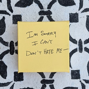 May include: A yellow canvas with black handwritten text that reads "I'm sorry I can't Don't hate me - "