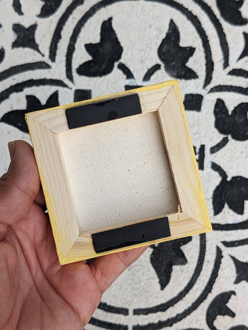 May include: The back of a small, yellow-painted wooden canvas frame with black tape on the edges. The canvas is white and the frame is made of wood.