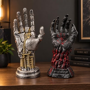 May include: Two hand sculptures on circular bases. The left is a silver and gold mechanical robotic hand with visible joints and cables. The right is a dark grey hand covered in small red skulls with a red symbol on the palm.