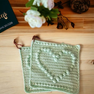 May include: Two green crocheted pot holders with a heart-shaped design. The pot holders are made with a textured stitch that creates a raised, bumpy effect.