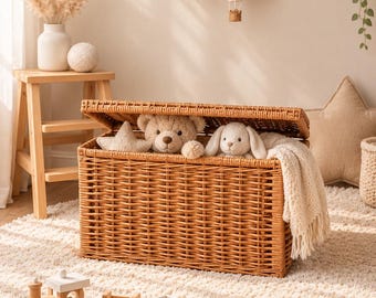 May include: A rectangular woven wicker storage chest with an open lid, containing a plush teddy bear, a plush rabbit, and a cream-colored knit blanket. The chest is made of light brown natural fibers and features a sturdy, boxy construction.