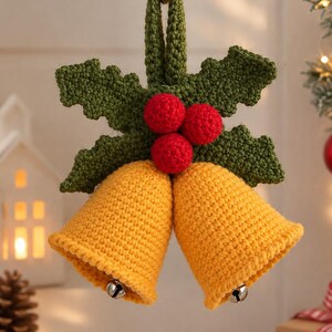 May include: A crocheted hanging ornament featuring two yellow bells suspended from a green crocheted holly leaf sprig with three red crocheted berries. Small silver metal jingle bells are attached inside each yellow bell.