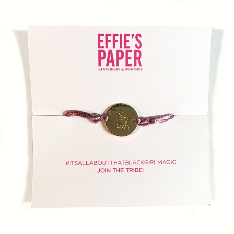 May include: A pink string bracelet with a gold charm that says "Black Girl Magic". The bracelet is on a white card with the text "Effie's Paper Stationery & Whatnot" and "#itsallaboutthatblackgirlmagic JOIN THE TRIBE!"