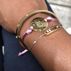 May include: A gold bracelet with a charm that says "hack your magic" and a pink string tied around it. The bracelet is on a person's wrist.