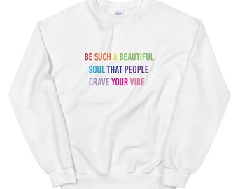 May include: White sweatshirt with the text "BE SUCH A BEAUTIFUL SOUL THAT PEOPLE CRAVE YOUR VIBE" in rainbow colors. The sweatshirt is a crew neck style and appears to be made of a soft material.