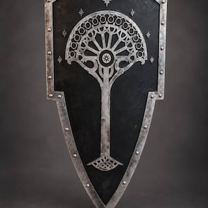 May include: A heater-style shield with a matte black surface and a metallic silver border secured by rivets. The center features a stylized silver tree emblem with a circular canopy and seven small star icons arranged in an arc above it.