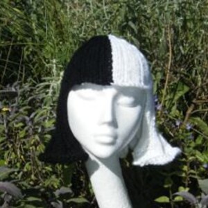 Puede incluir: Un gorro de punto negro y blanco con un diseño dividido, que se asemeja a un peinado. El gorro está en una cabeza de maniquí blanca.