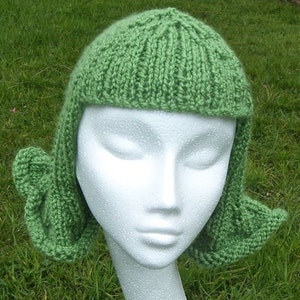 Peut inclure: Un bonnet en tricot vert avec des rabats d'oreilles. Le bonnet est sur une tête de mannequin blanche.