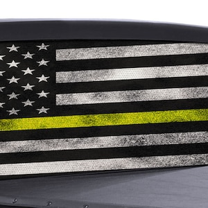 May include: A black and white American flag with a thin yellow stripe across the middle. The flag is displayed on the back window of a pickup truck.