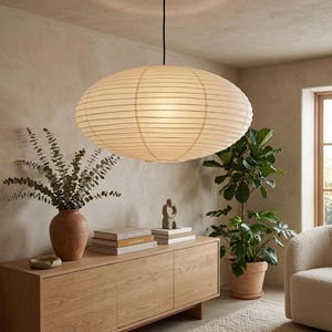 May include: A large, oval-shaped pendant light fixture made of off-white paper with horizontal ribbing. The lamp is suspended from a thin black cord and emits a soft, diffused glow, featuring a classic lantern-style construction.