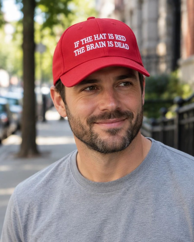 May include: A bright red baseball cap featuring white embroidered text on the front that reads, IF THE HAT IS RED THE BRAIN IS DEAD. The cap has a structured crown, a curved brim, and a button on top, constructed from a solid fabric material.