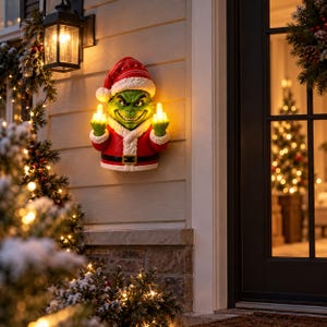 Könnte beinhalten: Eine Wanddekoration in Form einer grünen Figur, die einen rot-weißen Weihnachtsmannanzug und eine passende Mütze trägt. Die Figur hat einen schelmischen Gesichtsausdruck und leuchtende Finger, die eine Geste zeigen, sowie einen schwarzen Gürtel.