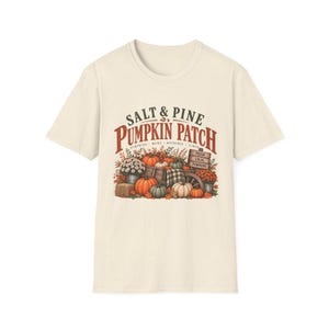 May include: A cream-coloured short-sleeve t-shirt featuring a graphic of a pumpkin patch with the text Salt & Pine Pumpkin Patch, Pumpkins, Mums, Hayrides, Cider, and Fresh Local Pumpkins. The design includes orange and green pumpkins.