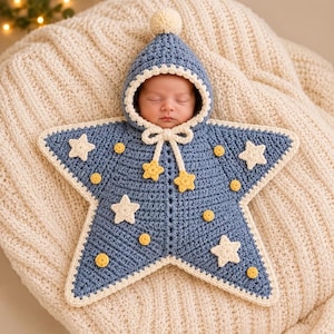 Könnte beinhalten: Ein sternförmiger Häkel-Babyschlafsack in Blau mit Kapuze, cremefarbenem Bommel, cremefarbener Umrandung sowie kleinen gelben und cremefarbenen Stern- und Kreisapplikationen. Er hat ein cremefarbenes Zugband mit zwei kleinen gelben Sternen.